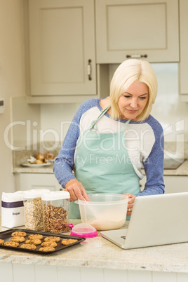 Happy blonde preparing dough following online recipe