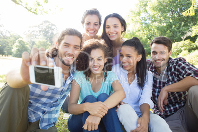 Smiling friends using media devices in park