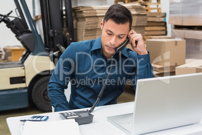 Warehouse manager using telephone and laptop