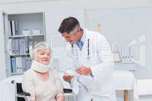 Doctor writing prescription for patient wearing neck brace