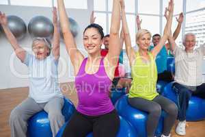 People sitting on exercise balls with hands raised
