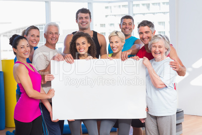 Happy people holding blank billboard at health club