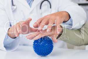 Doctor assisting female patient to hold massage ball