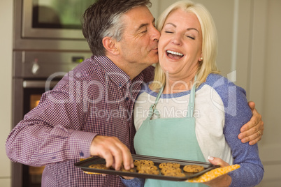 Mature blonde holding fresh cookies with husband kissing her