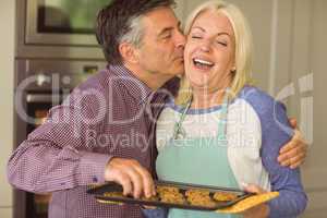 Mature blonde holding fresh cookies with husband kissing her