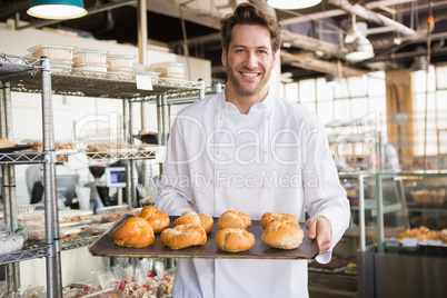 Cheerful baker holding tray of bread