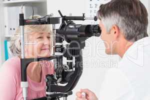 Optician examining senior female patient through slit lamp