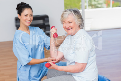Instructor assisting senior woman in lifting dumbbells