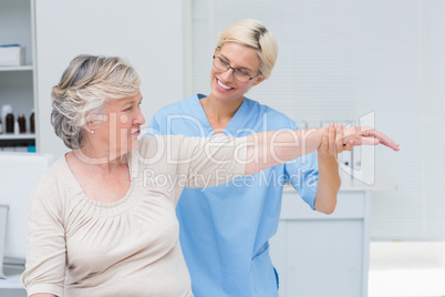 Nurse assisting senior patient in exercising at clinic