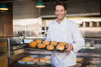 Portrait of smiling baker holding tray with bread