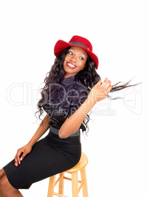 Black woman with red hat sitting on chair.