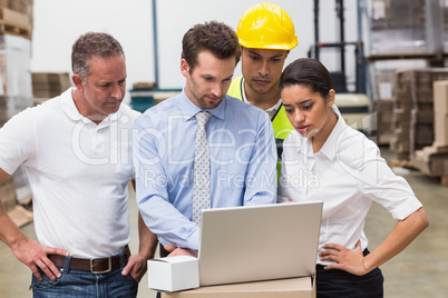 Warehouse managers and worker looking at laptop