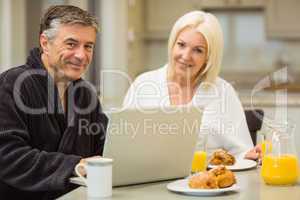 Mature couple having breakfast together man using laptop