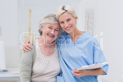 Friendly nurse with arm around senior patient in clinic