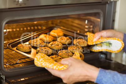 Woman taking tray of fresh cookies out of oven