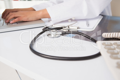 Doctor using laptop near stethoscope and clipboard