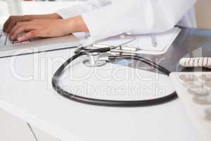 Doctor using laptop near stethoscope and clipboard