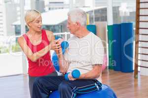 Female trainer assisting senior man in lifting dumbbells