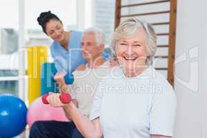 Senior woman lifting dumbbells while sitting with man and instru
