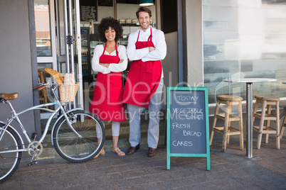 Smiling colleagues in red apron with arms crossed