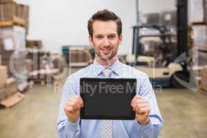 Warehouse manager showing tablet pc smiling at camera