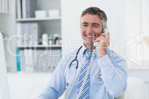 Confident male doctor using telephone in clinic