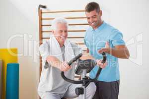 Senior man doing exercise bike with his trainer