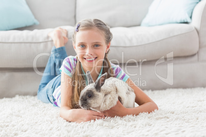 Happy girl with rabbit lying on rug in living room