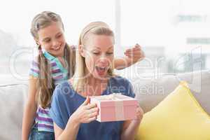 Happy girl surprising her mother with gift at home