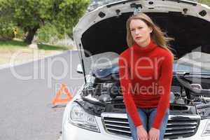 Annoyed young woman beside her broken down car