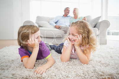 Siblings looking at each other while parents sitting on sofa