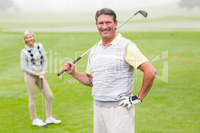 Happy golfer teeing off with partner behind him