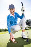 Smiling lady golfer kneeling on the putting green