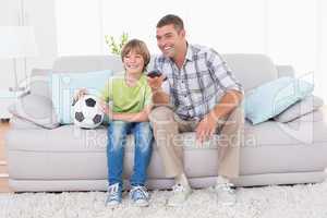 Father and son watching soccer match on sofa