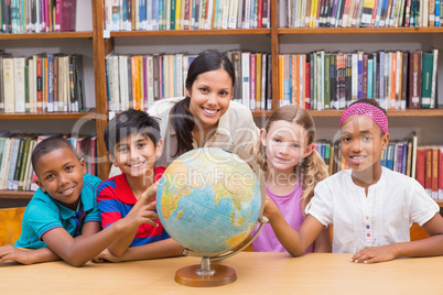 Cute pupils and teacher looking at globe in library