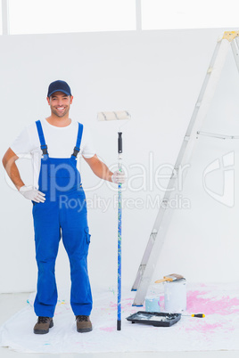 Handyman in overalls holding paint roller at home