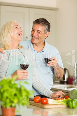 Happy mature couple having red wine while making dinner