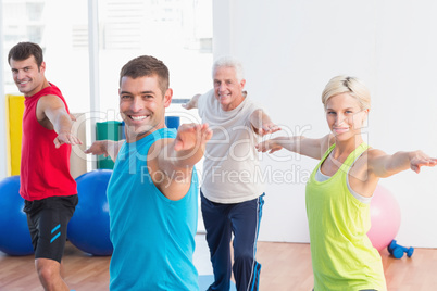 Happy people doing warrior pose in yoga class