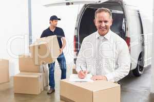 Smiling manager standing behind stack of cardboard boxes