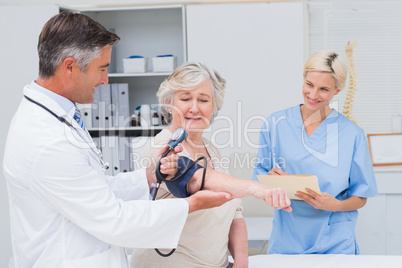 Doctor checking patients blood pressure while nurse noting it