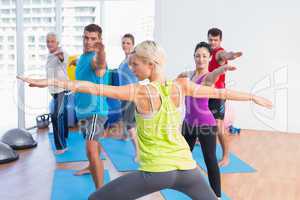 People practicing warrior pose in fitness club