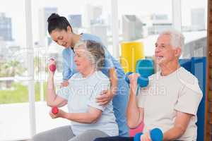 Instructor assisting senior woman in lifting dumbbells by man