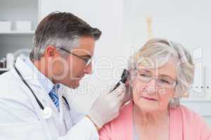 Doctor examining female patients ear with otoscope