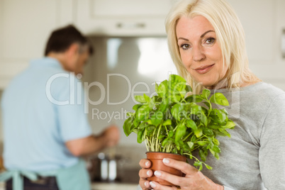 Mature blonde smiling at camera holding basil plant