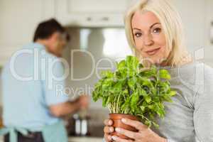 Mature blonde smiling at camera holding basil plant