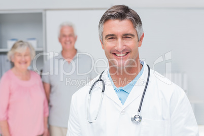 Doctor smiling with senior couple in background at clinic
