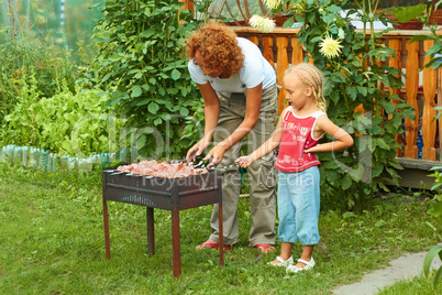 Little girl helping her mother to cook shish kebab