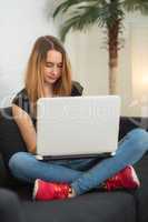 Teenager sitzt mit Laptop auf dem Sofa