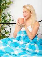 Frau mit Kaffeebecher im Bett riecht an der Tasse