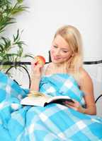 Blonde Frau mit Apfel und Buch im Bett